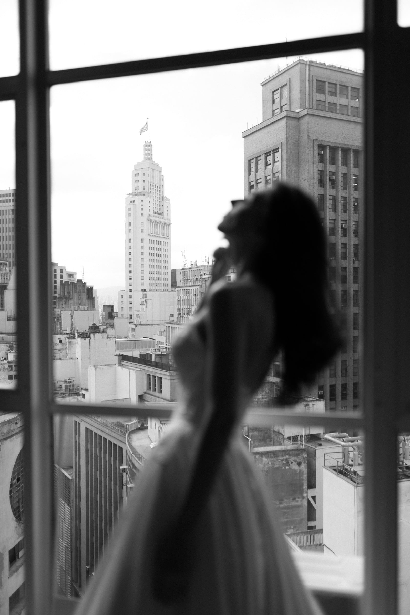 Noiva em silhueta diante de uma janela com vista para São Paulo, em fotografia preto e branco